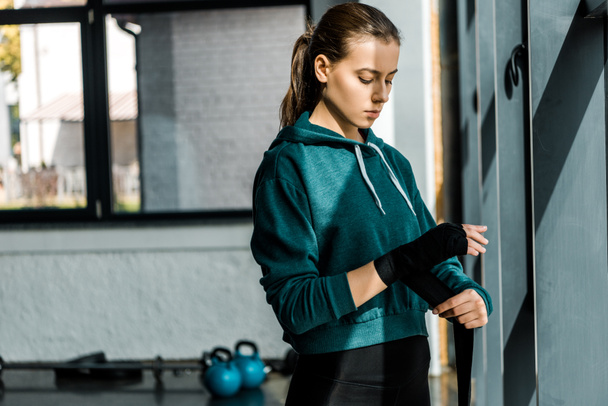 fokussierte Sportlerin zieht Sporthandschuhe im Fitnessstudio an - Foto, Bild