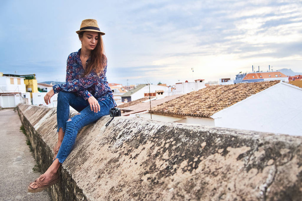Young attractive long-haired woman tourist in hat enjoying her vacations in Spain with panoramic view of small Spanish town Denia. - Фото, изображение