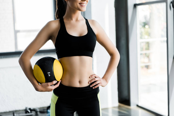cropped view of  beautiful smiling sportswoman holding medicine ball at gym - Фото, изображение