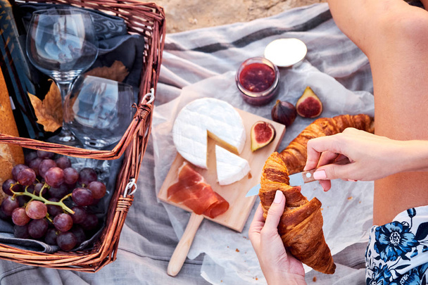 Top view of beautiful romantic picnic composition with croissants, bread, jam, cheese, figs and jamon. Young woman preparing food on picnic. - Photo, Image