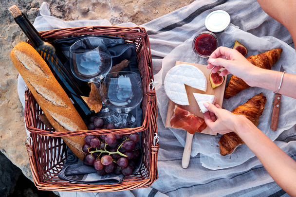 Top view of beautiful romantic picnic composition with croissants, bread, jam, cheese, figs and jamon. Young woman preparing food on picnic. - Foto, immagini
