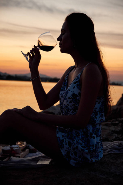 Young woman silhouette drinking wine on the beach at sunset. Picnic on the beach. - Valokuva, kuva