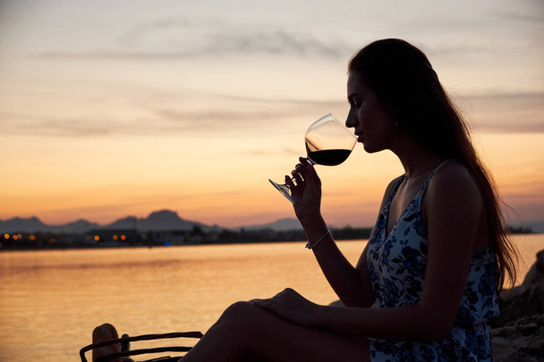 Young woman silhouette drinking wine on the beach at sunset. Picnic on the beach. - Φωτογραφία, εικόνα