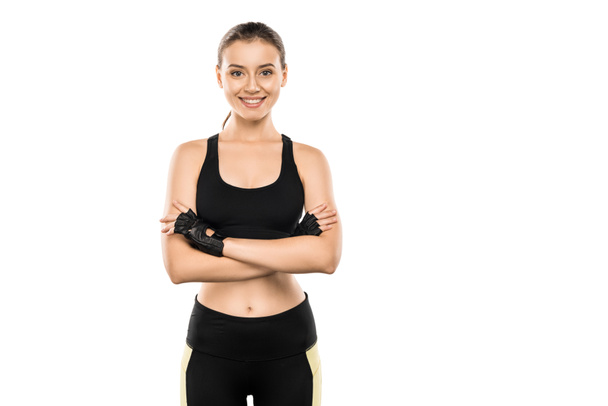 glimlachend Sportvrouw in Gewichtheffen handschoenen met armen gekruist kijken camera geïsoleerd op wit - Foto, afbeelding