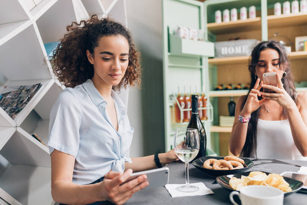 duas mulheres jovens bebendo em casa depois do trabalho usando telefone inteligente celebrando o sucesso, depois do trabalho, conceito relaxante
 - Foto, Imagem