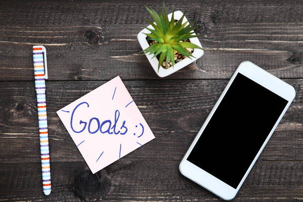 Goals on paper with smartphone, pen and green plant - Фото, изображение