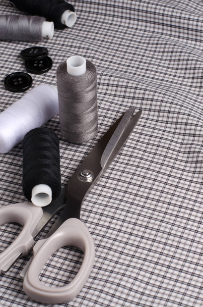Tools and accessories for sewing. Sewing thread, scissors, buttons on gray textile background. Vertical photo - Photo, Image