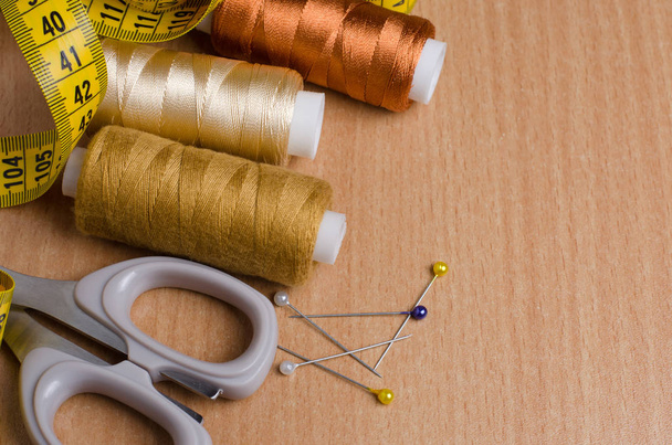 Tools and accessories for sewing. Sewing thread, scissors, pins, tailor tape on a wooden table. Close up - Photo, Image