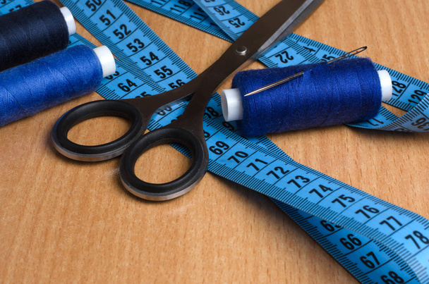 Tools and accessories for sewing. Sewing thread, scissors, tailor tape on a wooden table. Close up - Photo, Image