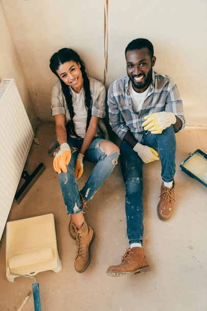 high angle view of couple sitting on floor and looking at camera during renovation of home - Foto, Imagem