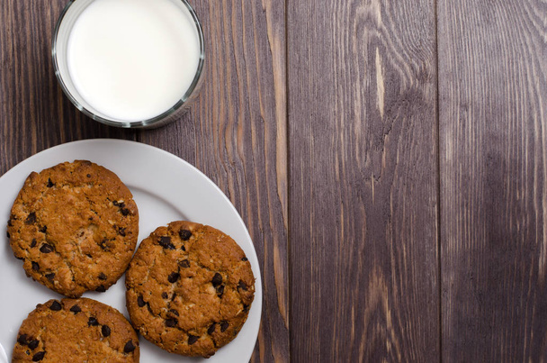 Homemade oatmeal cookies on a white plate and milk. Wooden background. Flat top view. Space for text - Foto, immagini