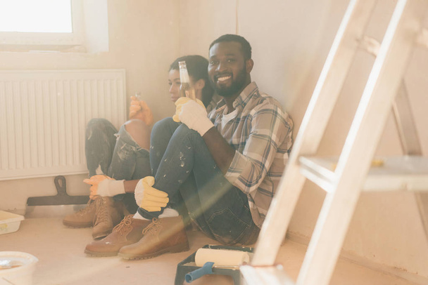 happy young couple relaxing on floor with beer while making renovation of home - Foto, immagini
