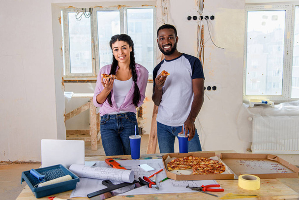 sorridente giovane coppia mangiare pizza mentre si effettua la ristrutturazione di casa
 - Foto, immagini