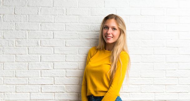 Happy blonde young girl on white brick wall background - Fotografie, Obrázek