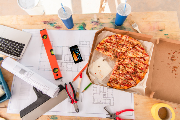 pohled shora box s pizza, nástroje a smartphone s grafy na obrazovce na stavební plán - Fotografie, Obrázek