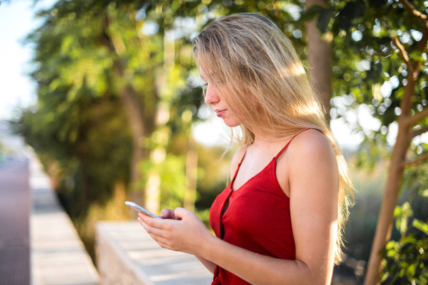 Jong blond meisje verzenden van een bericht of e-mail met de mobiele telefoon in buiten - Foto, afbeelding