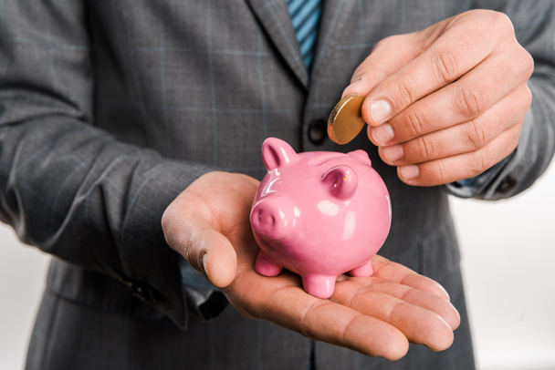 close-up partial view of businessman holding piggy bank and coin isolated on white - Foto, afbeelding