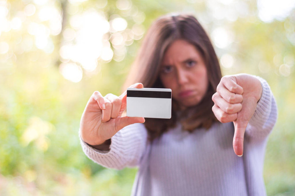 Νέοι ή λυπημένος Ευρωπαία γυναίκα ή κορίτσι Καυκάσιος κρατώντας μια πιστωτική ή χρεωστική κάρτα και κάνοντας μια αρνητική χειρονομία με το άλλο χέρι που δείχνει ότι δεν έχει χρήματα και έχει περάσει όλα - Φωτογραφία, εικόνα