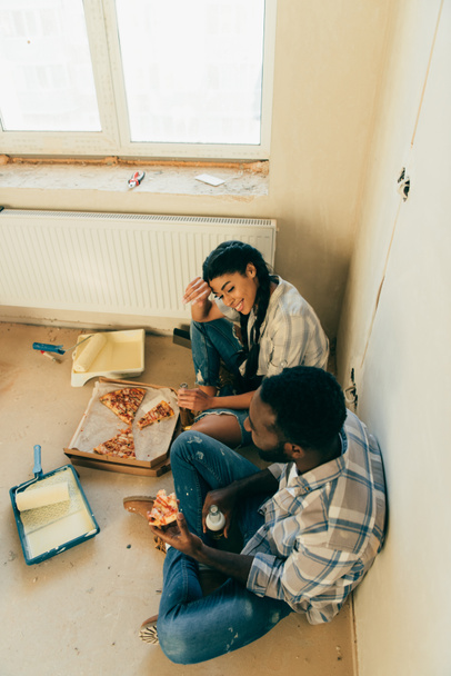 ピザを食べて、自宅改装中にビールを飲むアフリカ系アメリカ人のカップルのハイアングル - 写真・画像