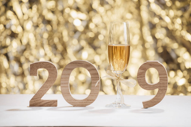 Искрящийся новогодний фон с бокалом шампанского и деревянными номерами 2019
 - Фото, изображение
