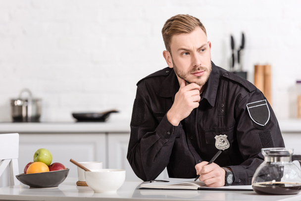 thoughtful policeman sitting at kitchen table - Фото, изображение