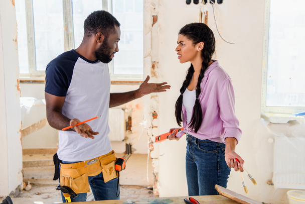 side view of irritated woman talking to boyfriend doing shrug gesture during renovation at home - Photo, Image