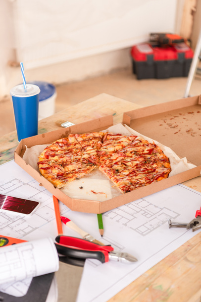 selective focus of pizza, soda, blueprint, tools and smartphone with graphs on screen on table - Фото, изображение
