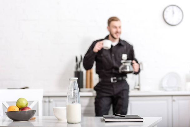 Notizbuch, Milchflasche, Obstschale auf Küchentisch und Polizist im Hintergrund - Foto, Bild