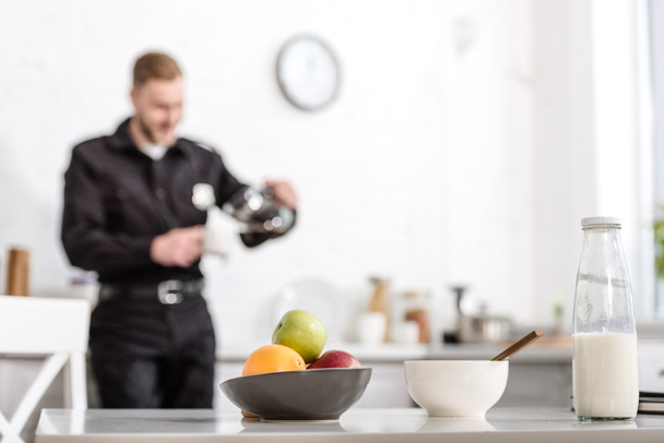 milk bottle, bowl of fruits on kitchen table and police officer at background - Photo, Image