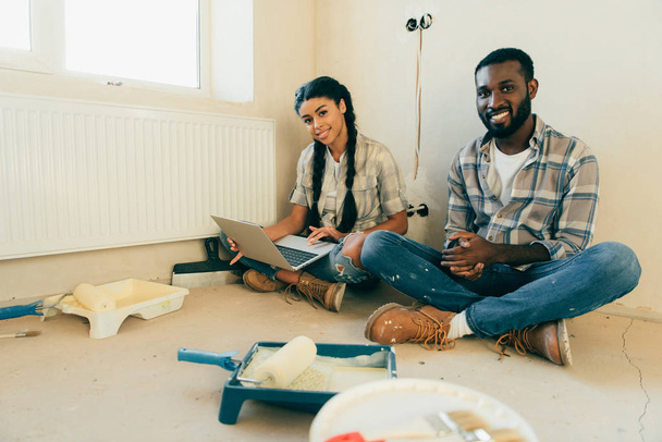 african american couple resting with laptop during renovation of new home - Фото, изображение