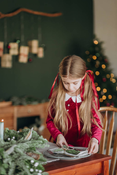 girl in a burgundy dress decorates a Christmas tree in a rustic room - Photo, Image