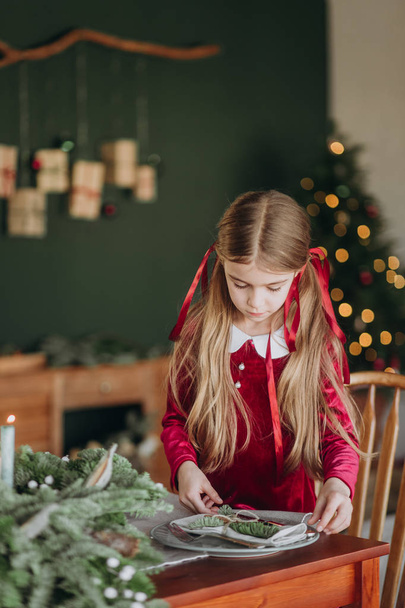 girl in a burgundy dress decorates a Christmas tree in a rustic room - Foto, Imagem