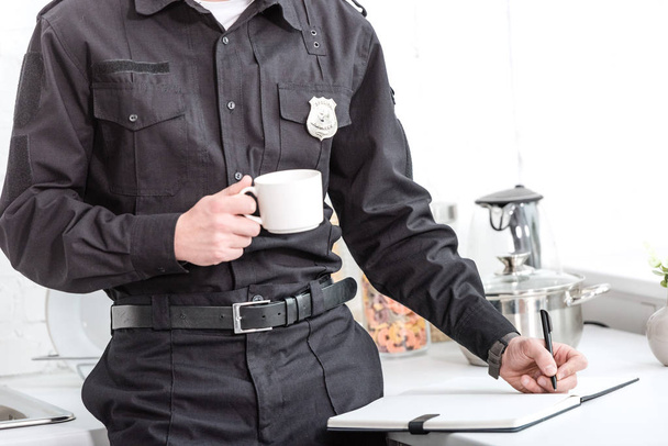 コーヒーを飲むと、台所のテーブルでノートを書く警察官 - 写真・画像