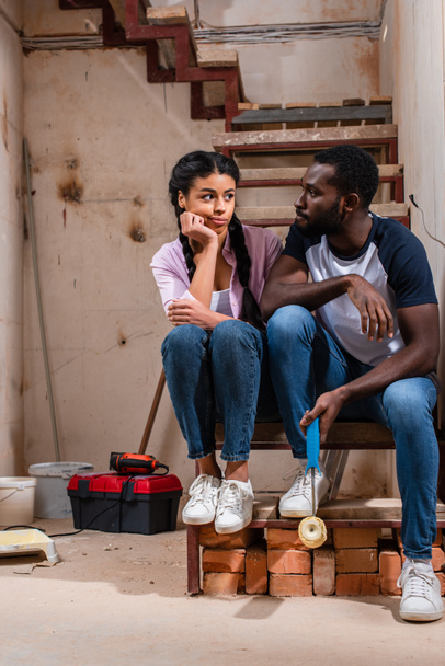 新しい家の改築時に階段の上に座って疲れの若いアフリカ系アメリカ人のカップル - 写真・画像