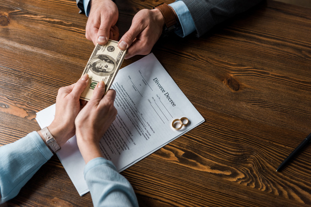 visão superior parcial da mulher dando dinheiro ao advogado sobre o decreto de divórcio com anéis de casamento
 - Foto, Imagem