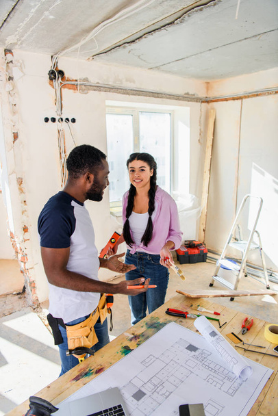 vista de alto ângulo do jovem casal afro-americano em pé perto da mesa com planta durante a renovação da casa
 - Foto, Imagem