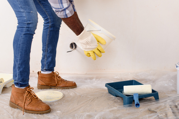 wykadrowanego obrazu człowieka w rękawicach ochronnych nalewanie farby do rolki podajnika podczas remontu domu - Zdjęcie, obraz