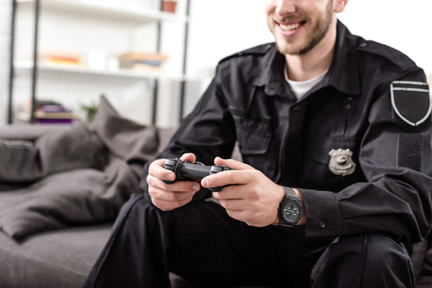 rajattu näkymä poliisi peliohjain istuu sohvalla ja pelaa videopeliä
 - Valokuva, kuva