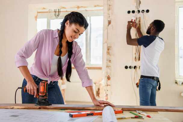 atractiva mujer afroamericana que trabaja con rompecabezas, mientras que su novio de pie detrás durante la renovación en casa
 - Foto, Imagen