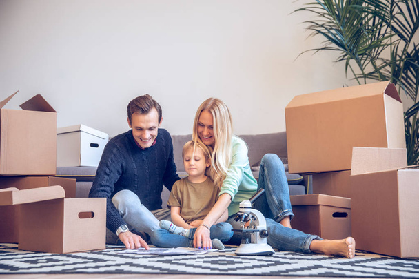 Photo of happy man,woman and small boy sitting on floor among cardboard boxes - Photo, Image
