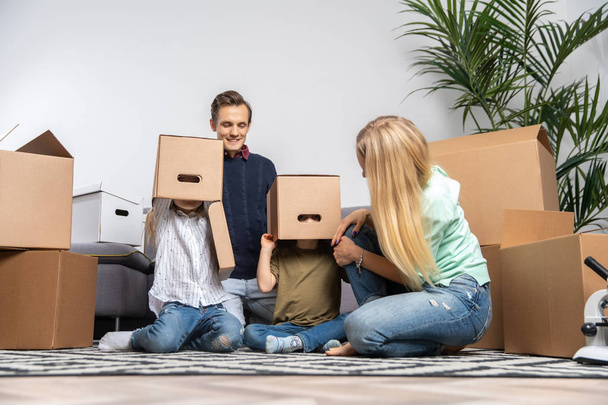 Picture of parents and children with cardboard boxes on their heads in new apartment - Foto, Imagen