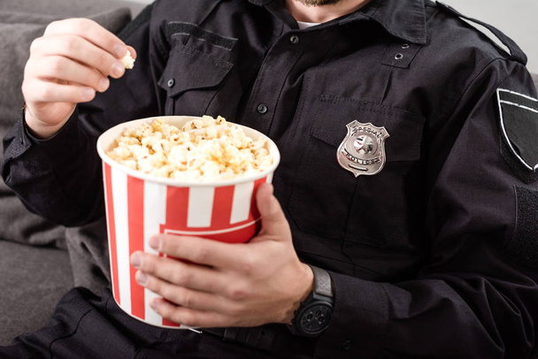 обрезанный вид полицейского, сидящего на диване и поедающего попкорн
 - Фото, изображение