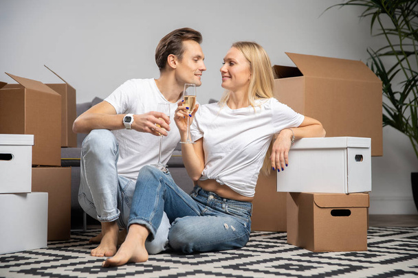 Image of happy couple with champagne glasses sitting among cardboard boxes - Photo, Image