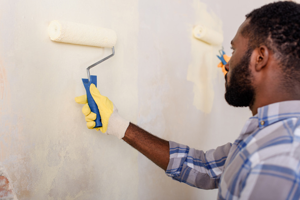 concentrated african american man painting wall by paint roller  - Photo, Image