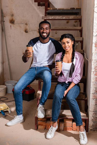 happy african american couple resting with disposable cups of coffee during renovation at new home - Foto, Imagem