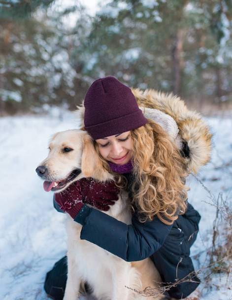 Oung όμορφη γυναίκα αγκαλιάζει golden retriever σκύλου στο χιόνι - Φωτογραφία, εικόνα