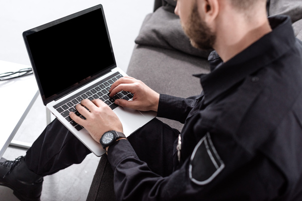 oříznutý pohled policejní důstojník sedící na gauči a psaní na klávesnici notebooku - Fotografie, Obrázek