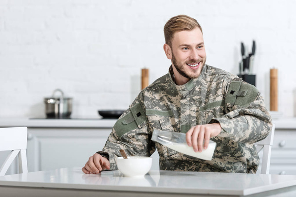 Guapo militar vertiendo leche en un tazón con copos de maíz en la mañana
 - Foto, Imagen