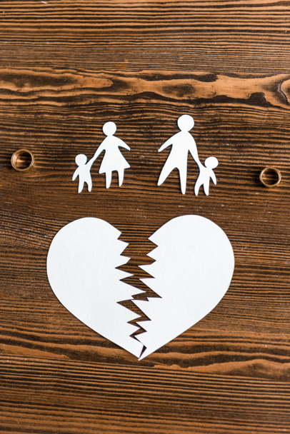bovenaanzicht van hart gescheurd met familie en verlovingsringen op houten tafel, echtscheiding concept - Foto, afbeelding