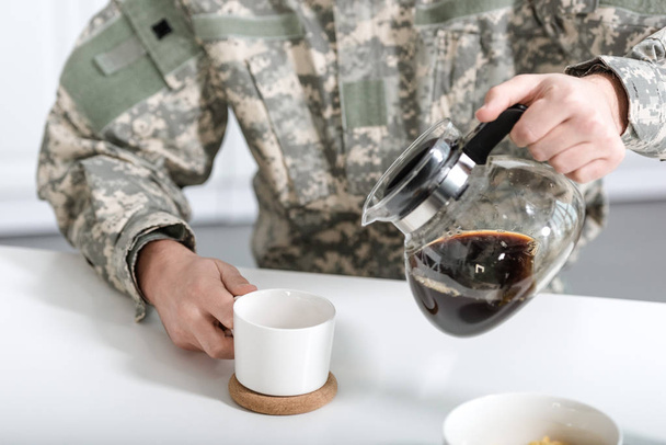 cropped view of man in camouflage uniform pouring coffee in cup from kettle - Foto, imagen